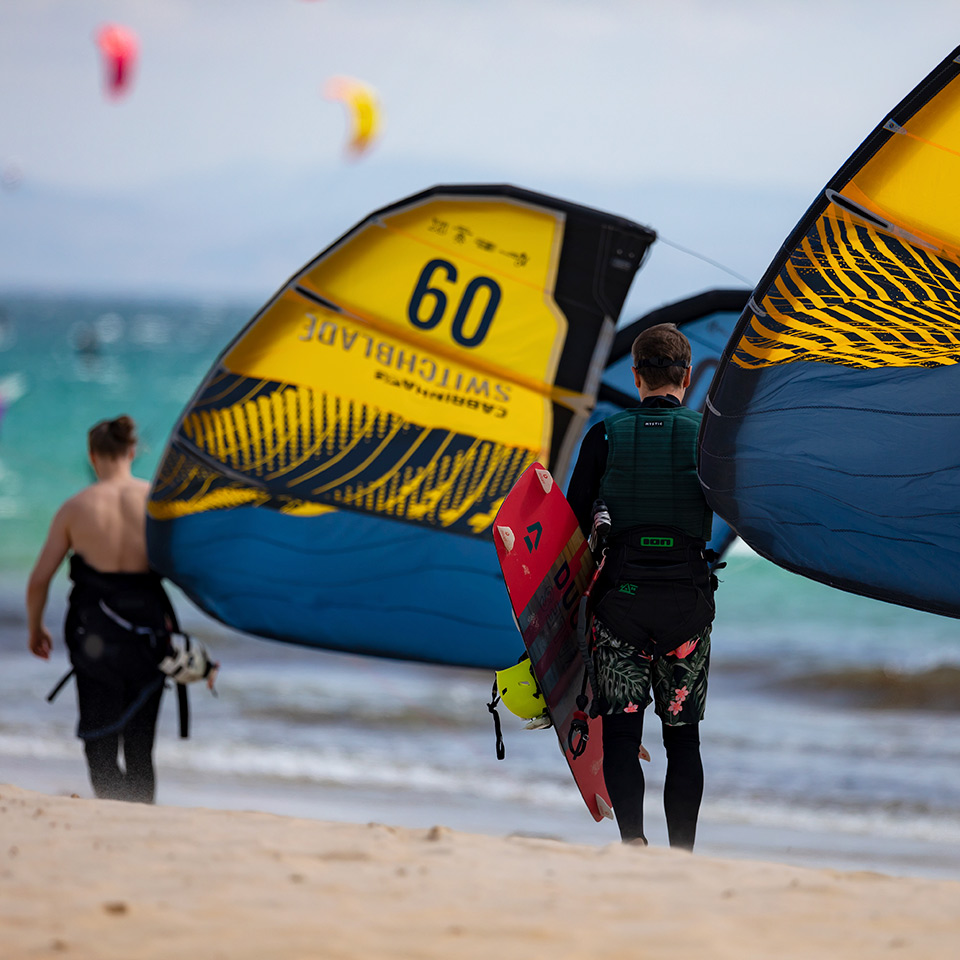 Chicos andando por la playa con cometas de kitesurf